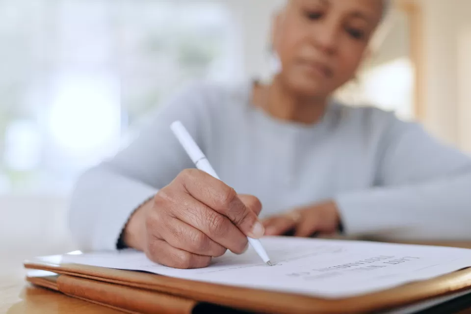 Older black woman writes on document with a pen.